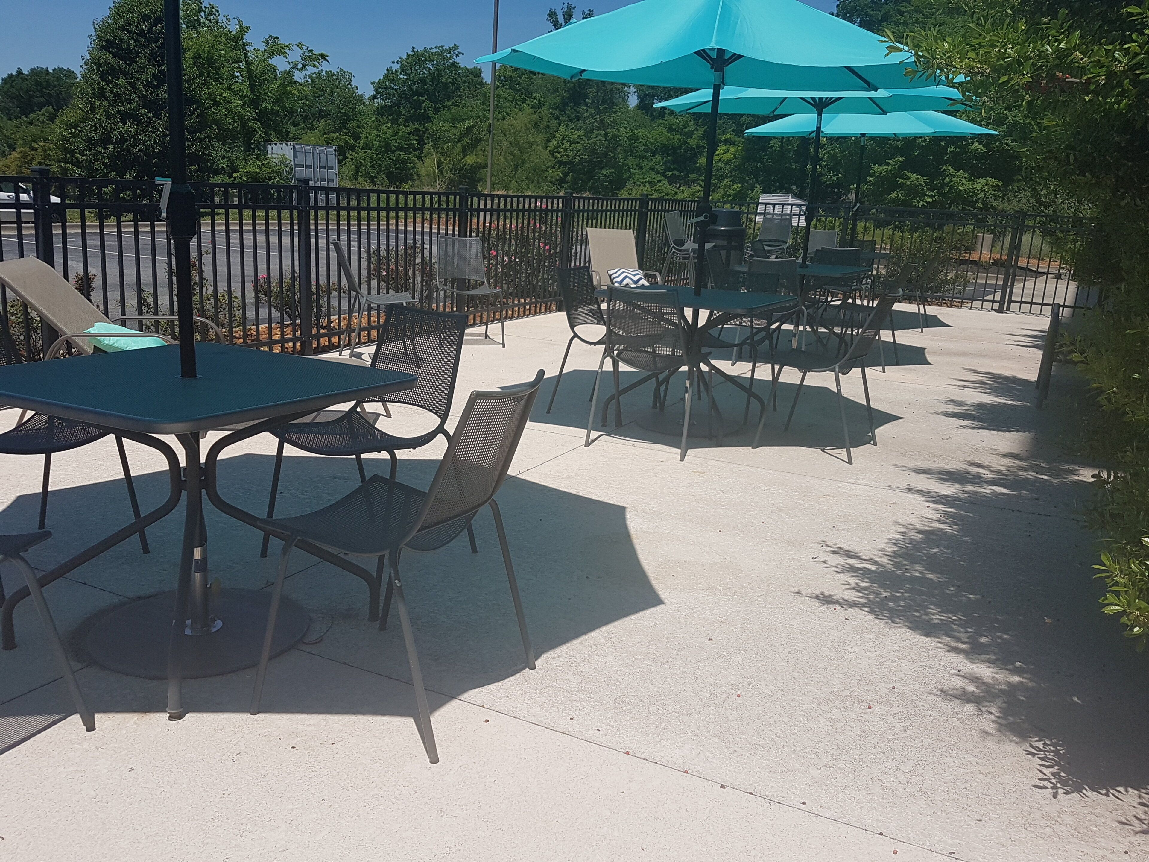 An outdoor patio area with tables and chairs, surrounded by a metal fence.