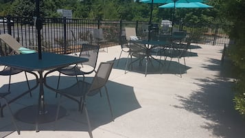 An outdoor patio area with tables and chairs, surrounded by a metal fence.