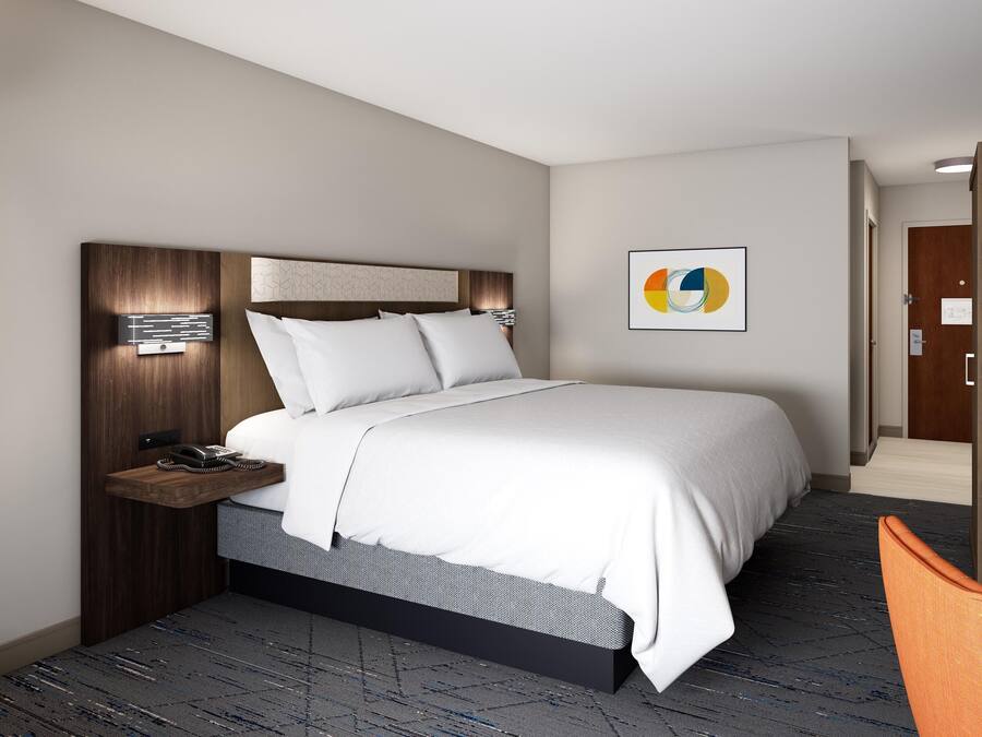 Habitación de hotel moderna con una cama grande, una mesita de noche con teléfono, un estante pequeño y una obra de arte colgada en la pared.