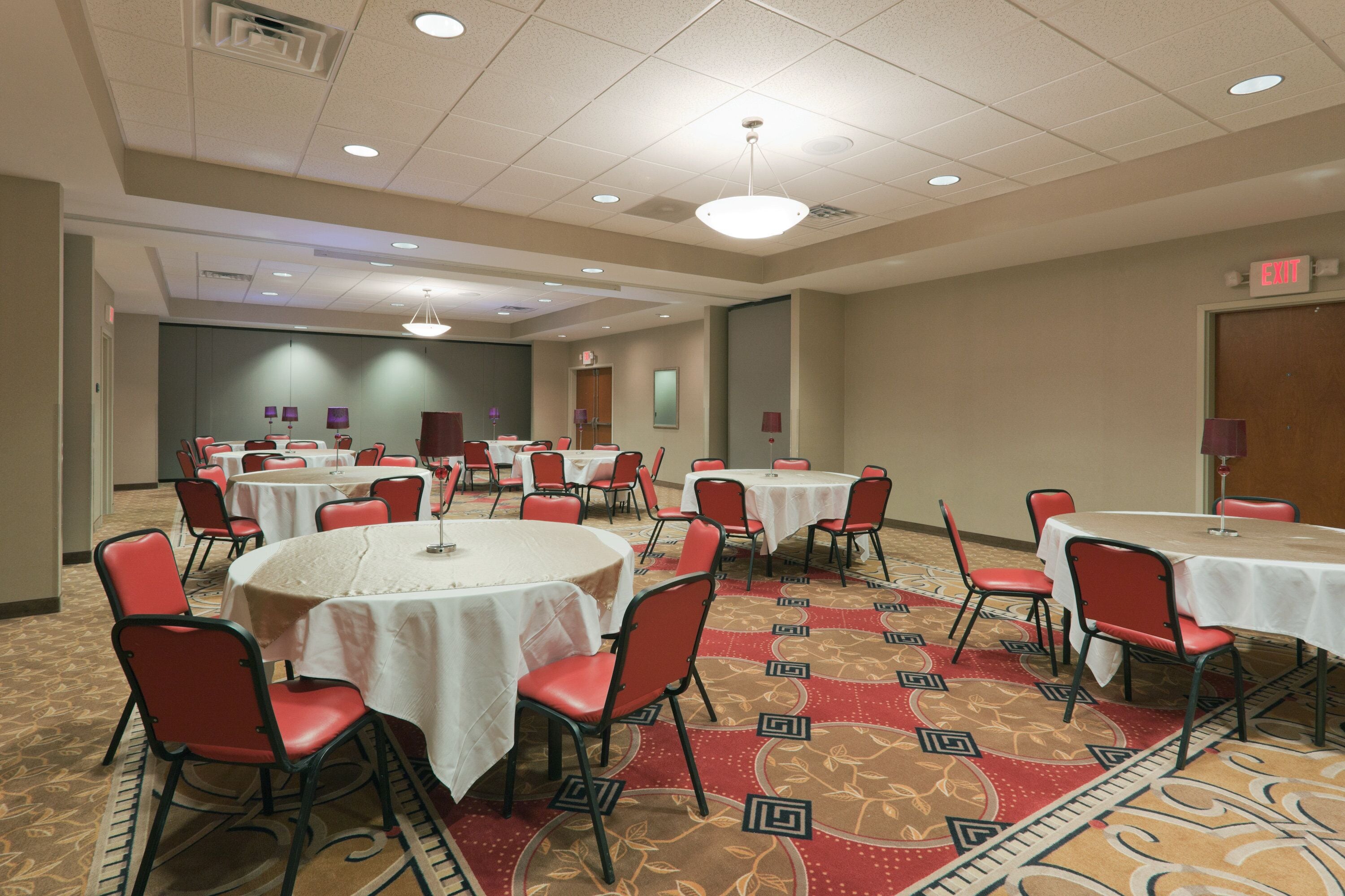 A conference room with multiple round tables, red chairs, and carpeted flooring.