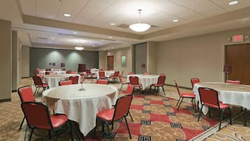 A conference room with multiple round tables, red chairs, and carpeted flooring.