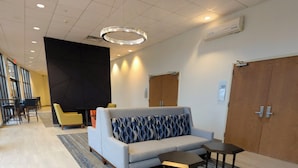 Un hall d’entrée moderne avec un canapé gris, des coussins à motifs, une petite table et un lustre.