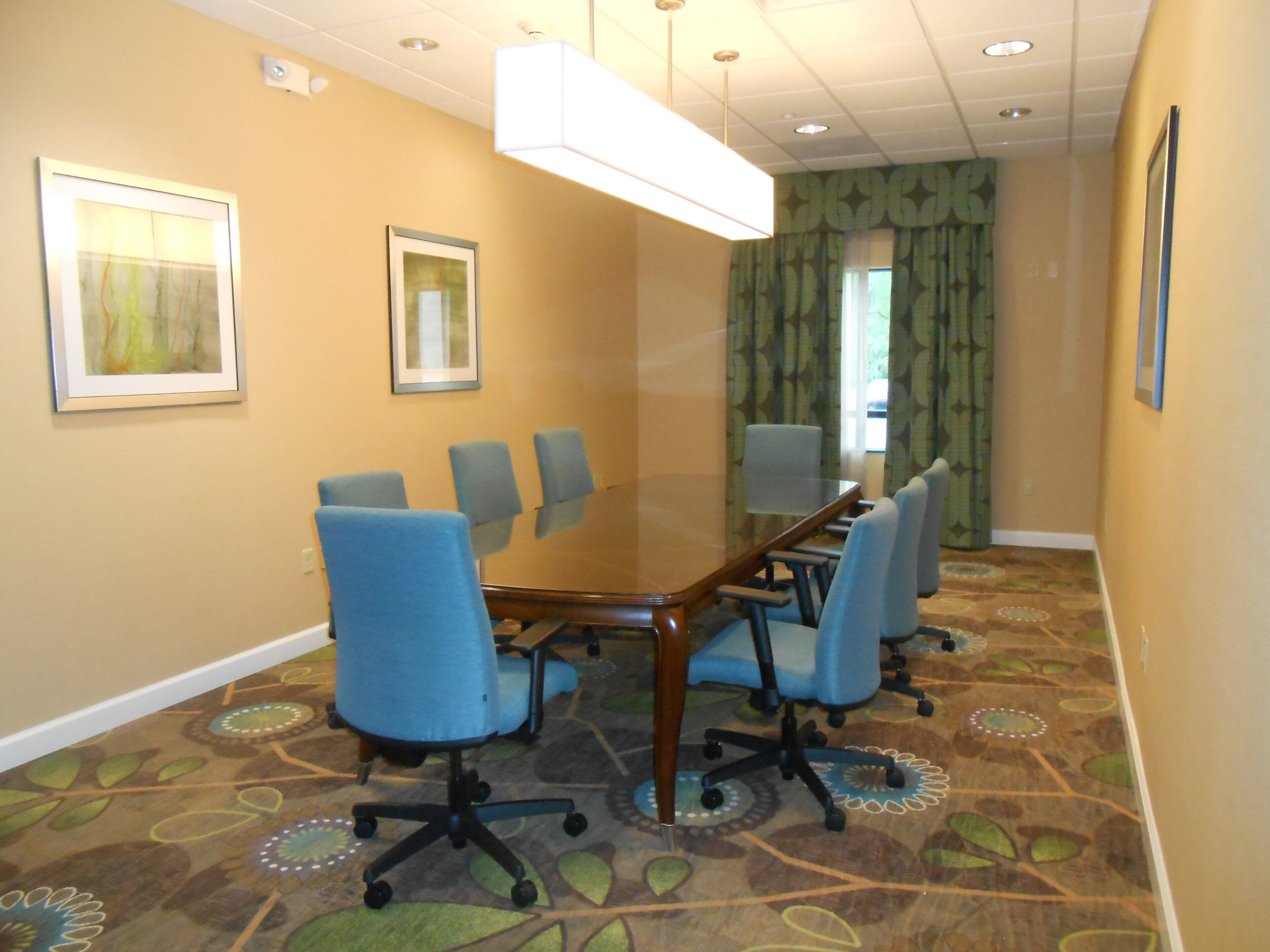A conference room with a glass table, blue chairs, patterned carpet, and framed pictures on the walls.