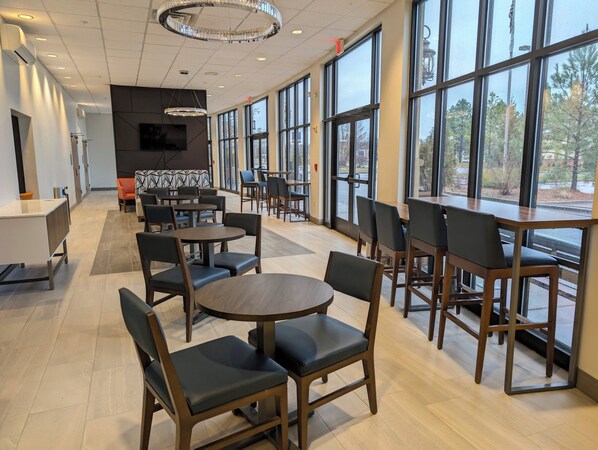 A modern dining area with round tables and chairs, large windows, and a chandelier.