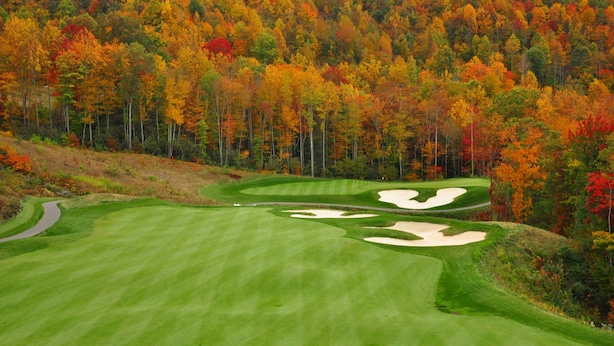 Un parcours de golf avec un chemin sinueux et des bunkers de sable, entouré d’arbres aux couleurs automnales.
