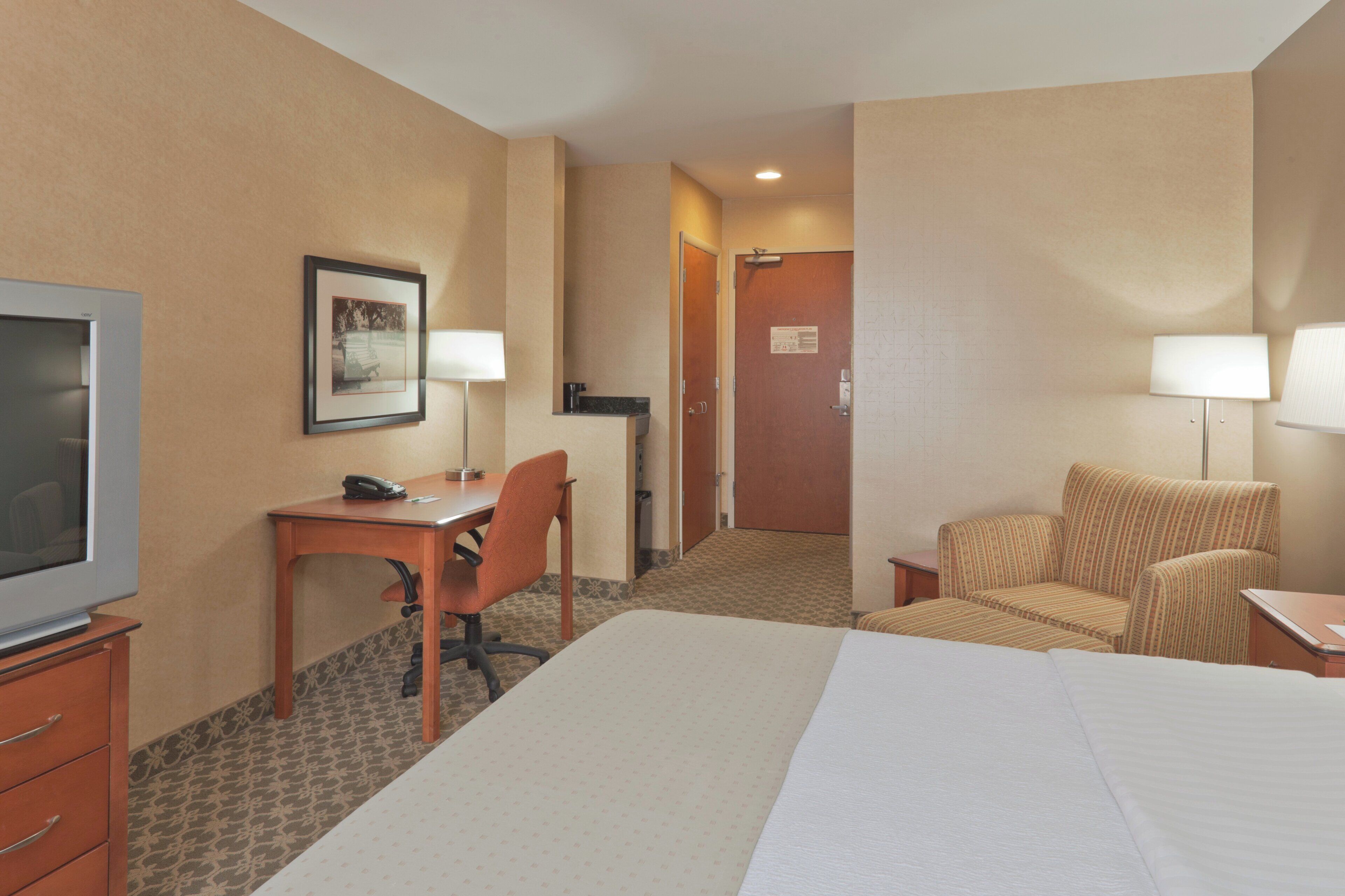 A hotel room with a bed, a desk, a chair, a television, and two lamps.