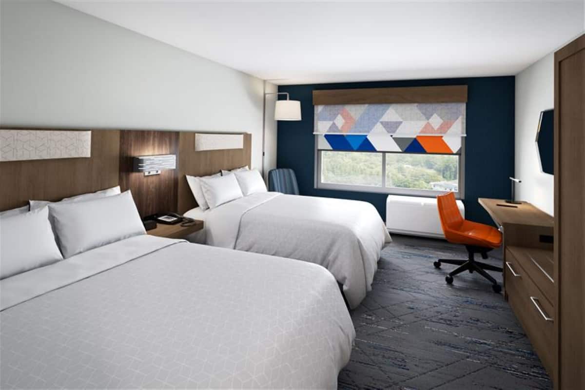 A hotel room with two beds, a desk, a chair, a nightstand, and a window with a view.