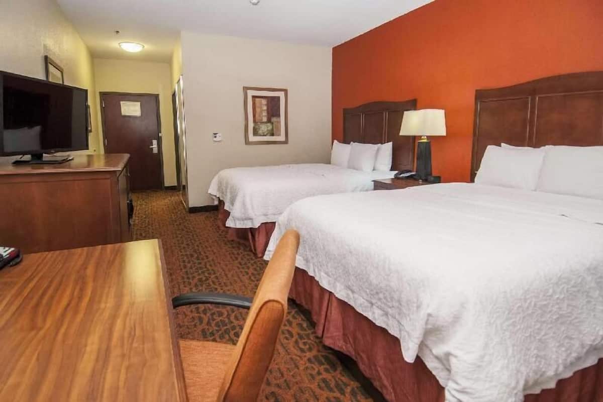 Una habitación de hotel con dos camas, un escritorio, un televisor y piso alfombrado.