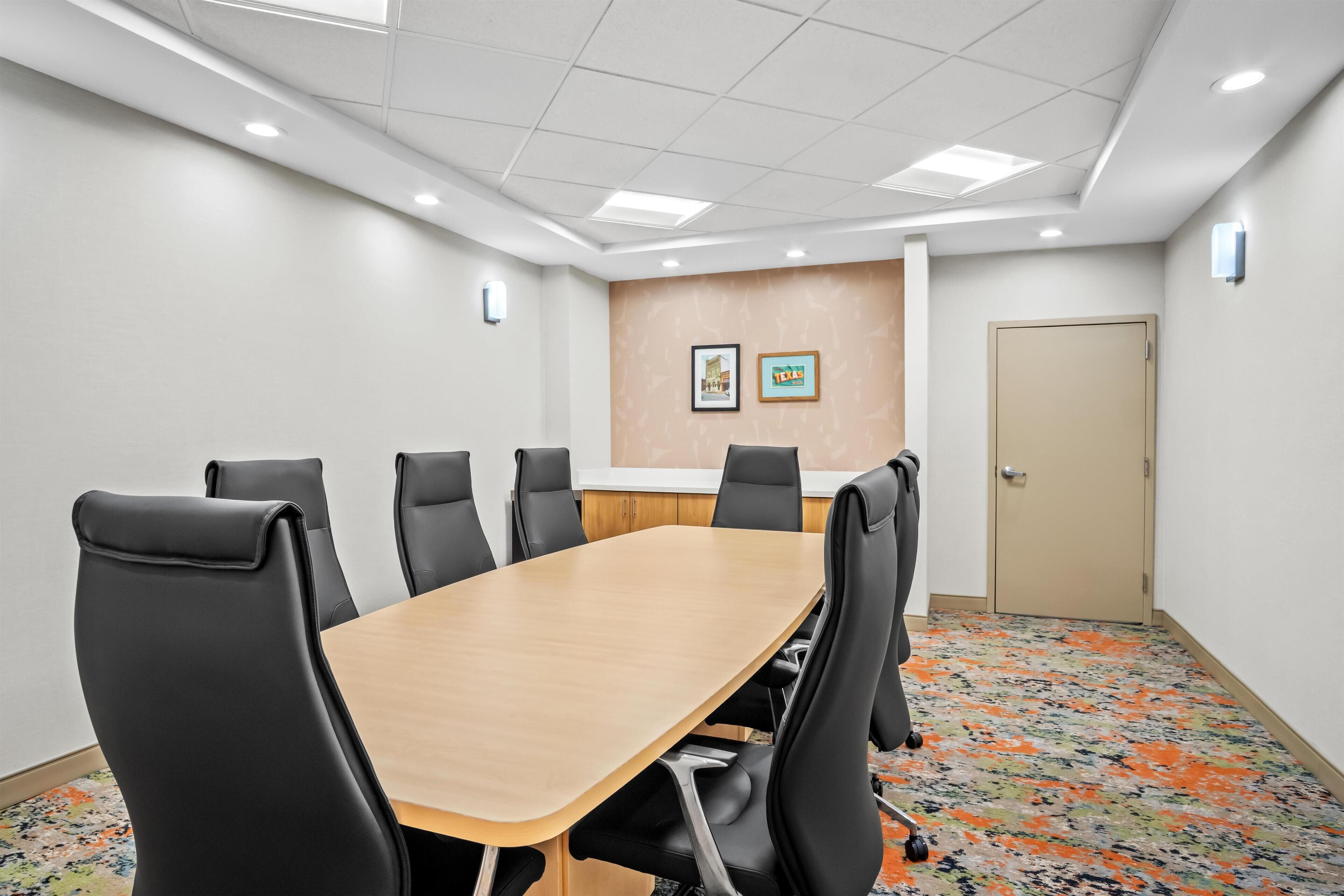 A conference room with a long table, black chairs, a wooden conference table, and a patterned carpet.