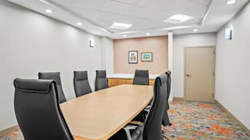 Una sala de conferencias con una larga mesa, sillas negras, una mesa de reuniones de madera y una alfombra estampada.