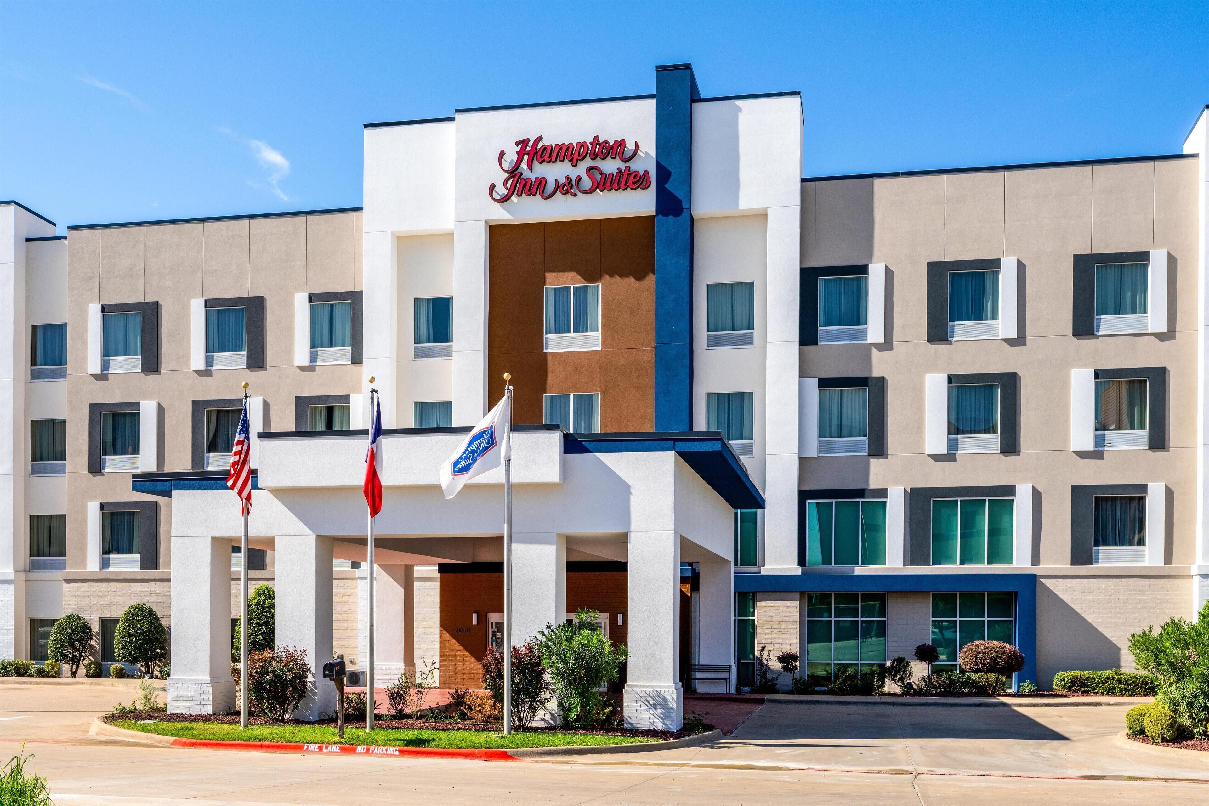 A Hampton Inn & Suites hotel with a modern facade, multiple windows, and a prominent entrance.