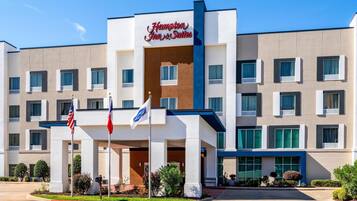 A Hampton Inn & Suites hotel with a modern facade, multiple windows, and a prominent entrance.