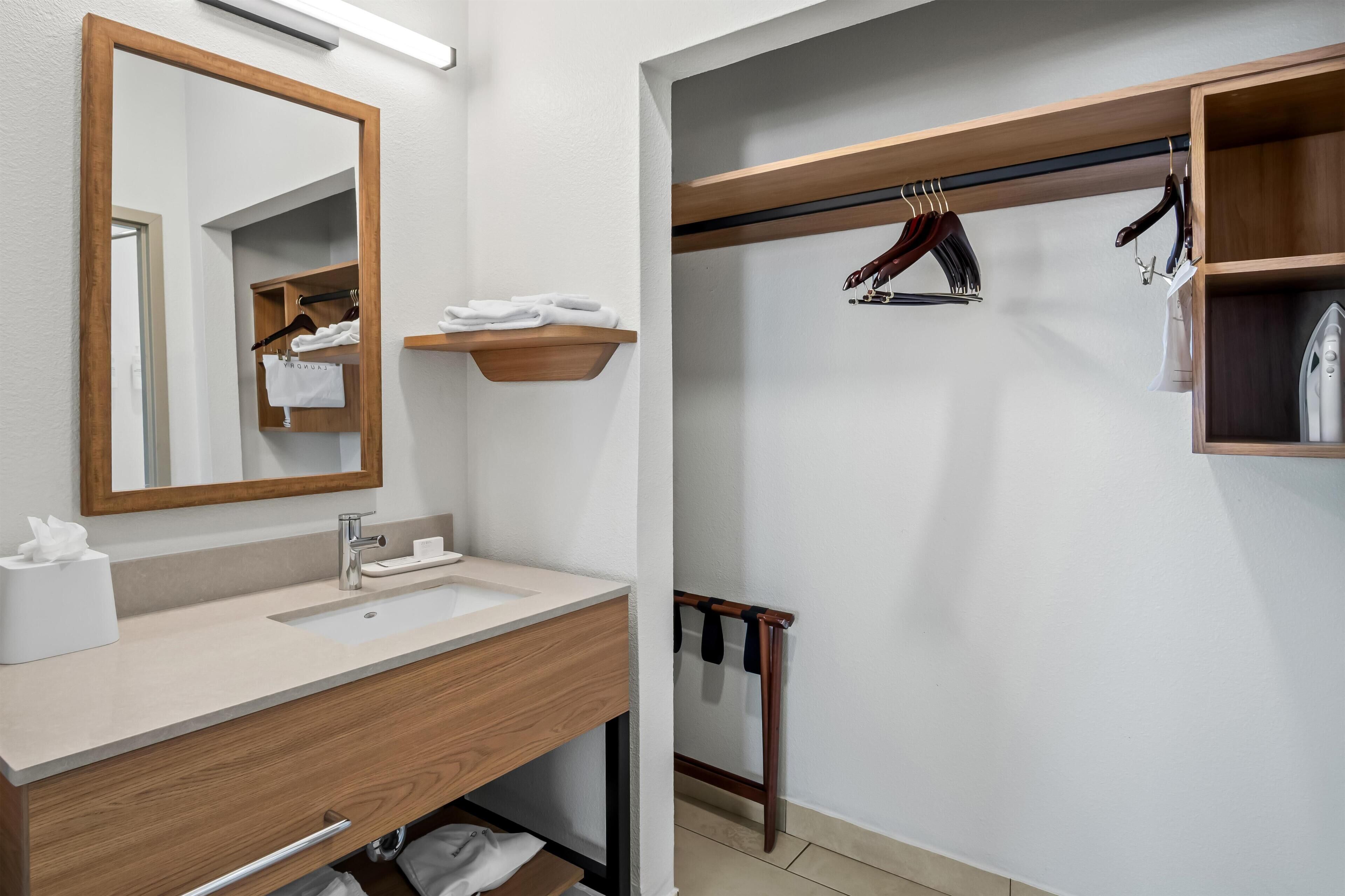 A modern bathroom with a wooden vanity, a large mirror, and a hanging rack for towels.
