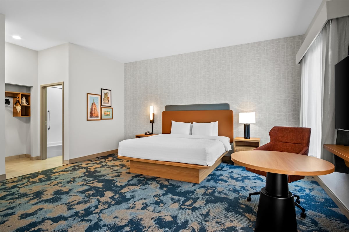Habitación de hotel con una cama grande, un escritorio, una silla, un televisor y una puerta que da a un baño.
