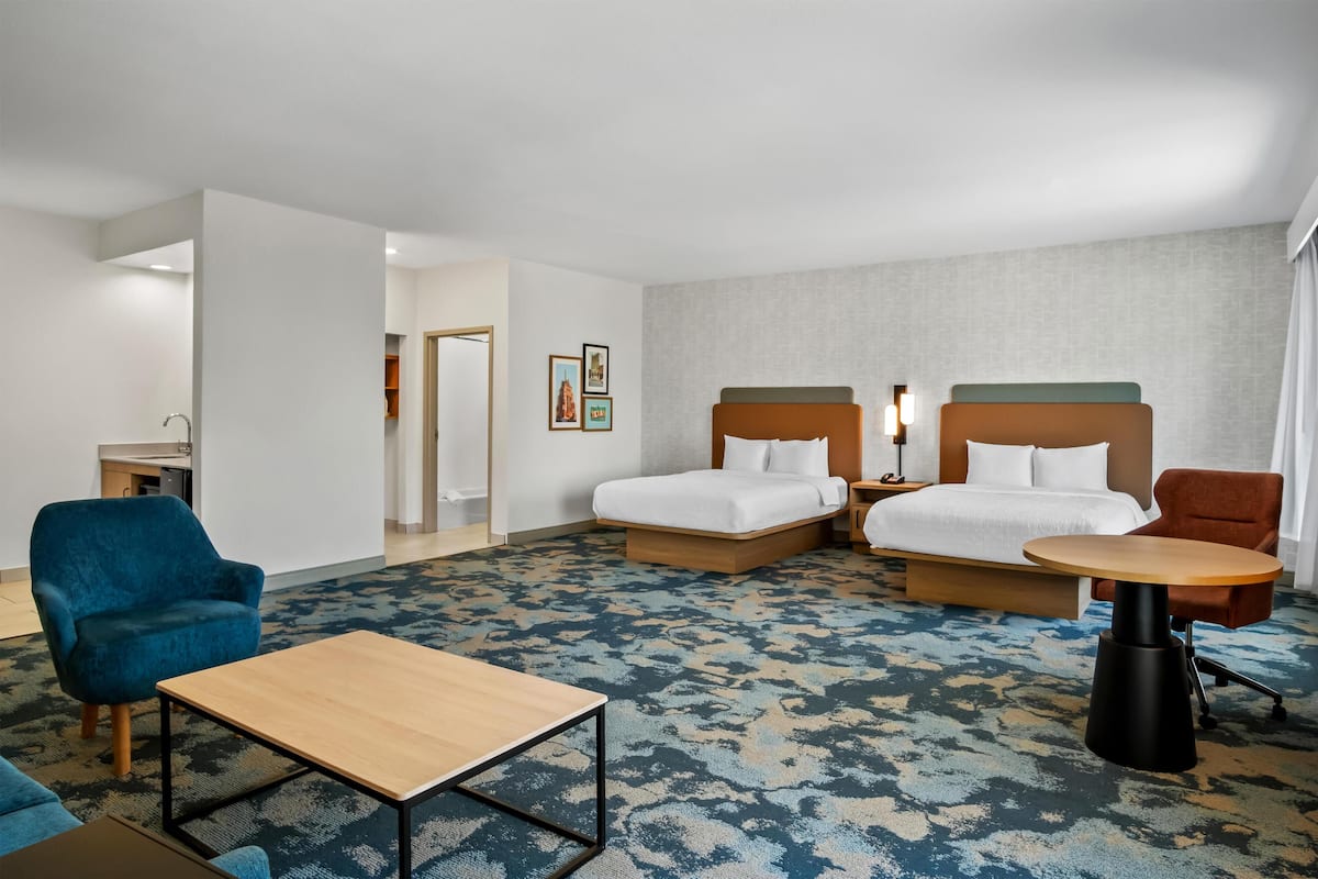 Una habitación de hotel con dos camas, un escritorio, una silla, un sofá y un baño.