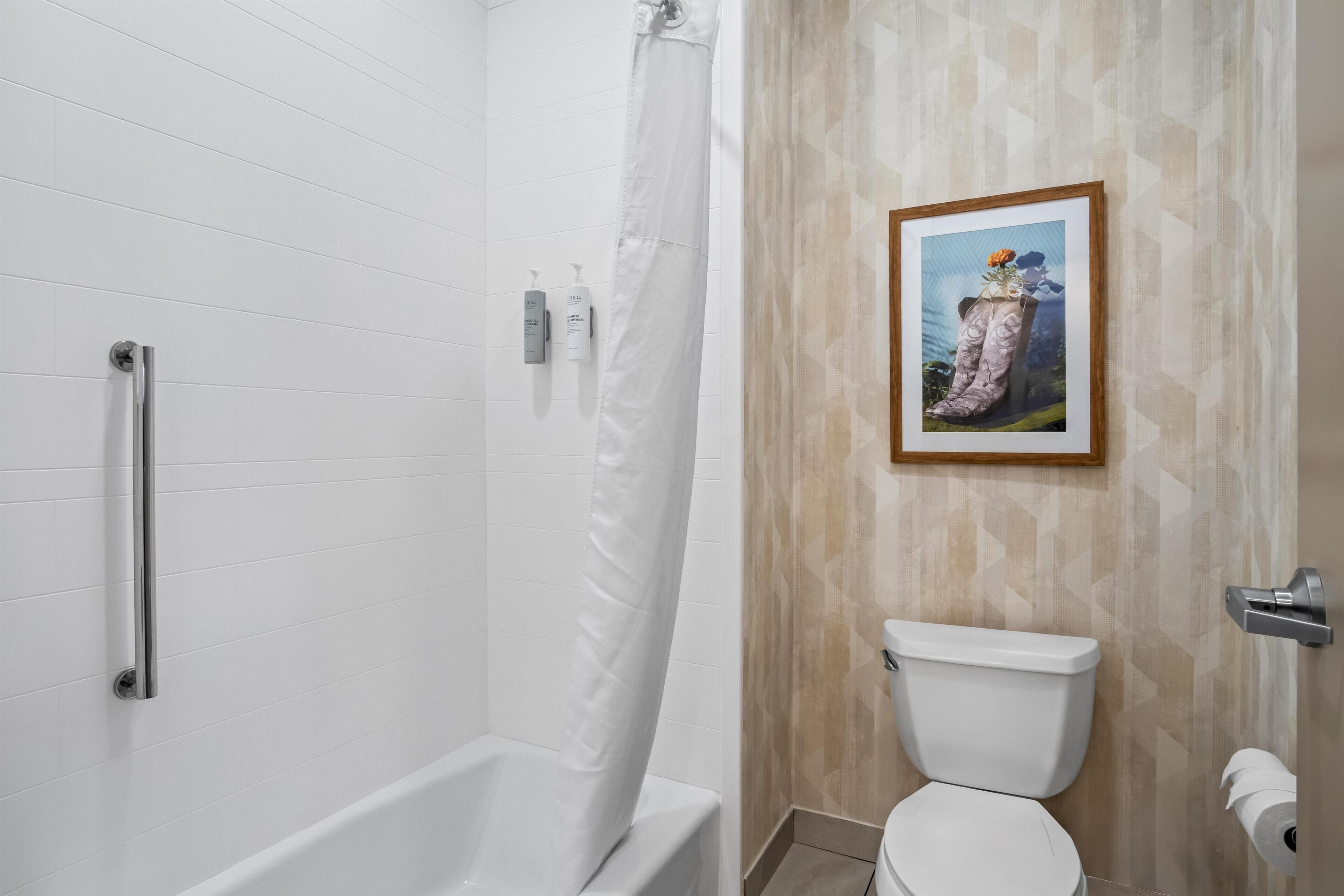 A bathroom with a white bathtub, a shower curtain, a toilet, and a framed picture on the wall.