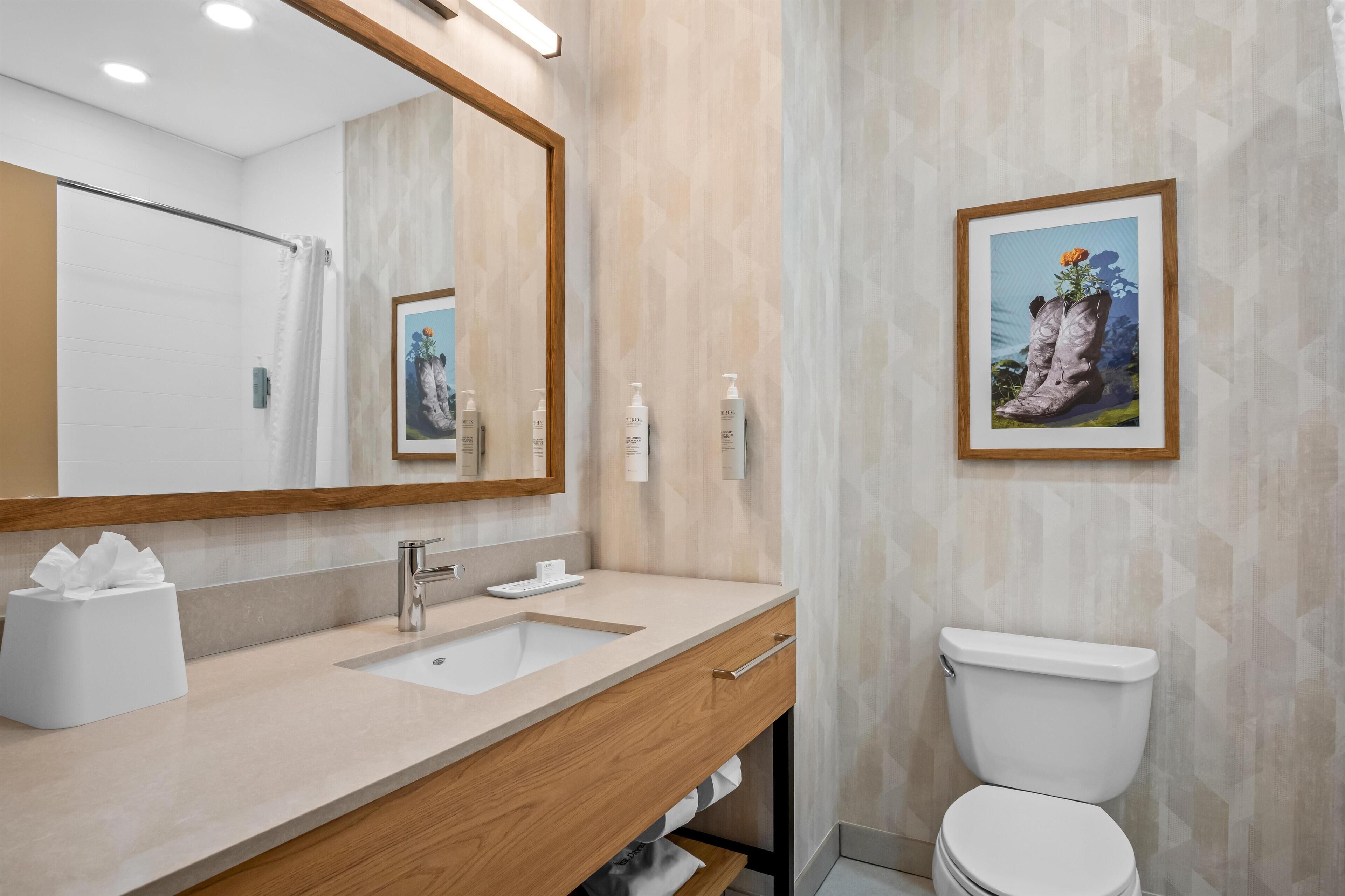 A modern bathroom with a wooden vanity, a large mirror, a sink, and a toilet.