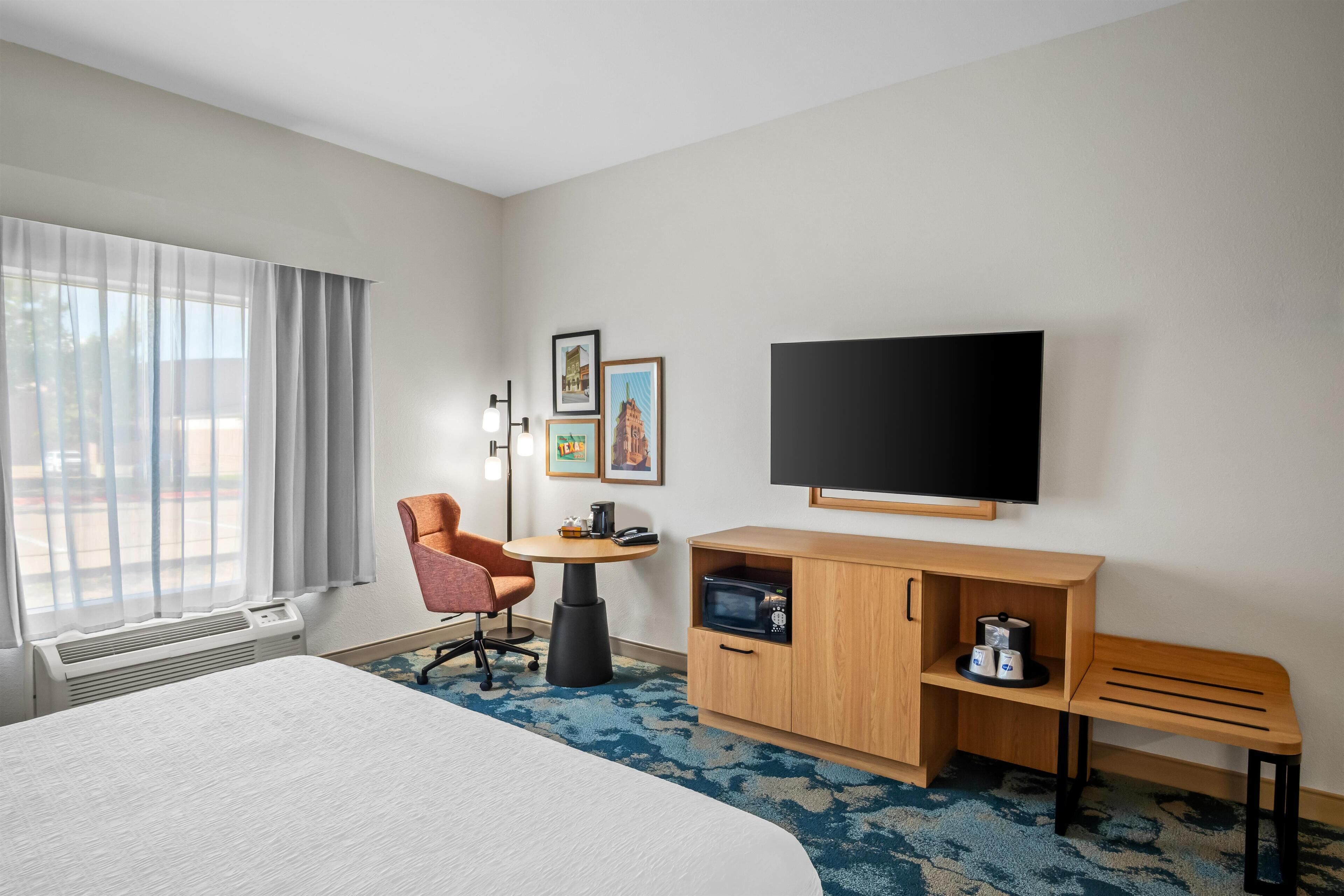 A hotel room with a large bed, a desk with a chair, a flat-screen TV, a coffee maker, and framed pictures on the wall.