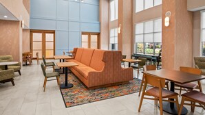 A spacious indoor area with a large orange sofa, wooden tables, and chairs, and a patterned rug. - Hampton Inn & Suites Waxahachie (Waxahachie)