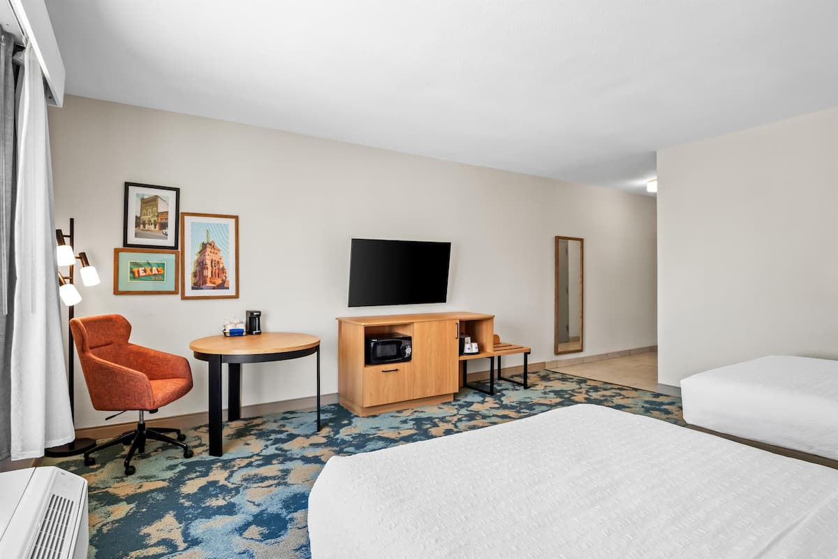 Una habitación de hotel con cama, escritorio, silla, televisor y microondas.