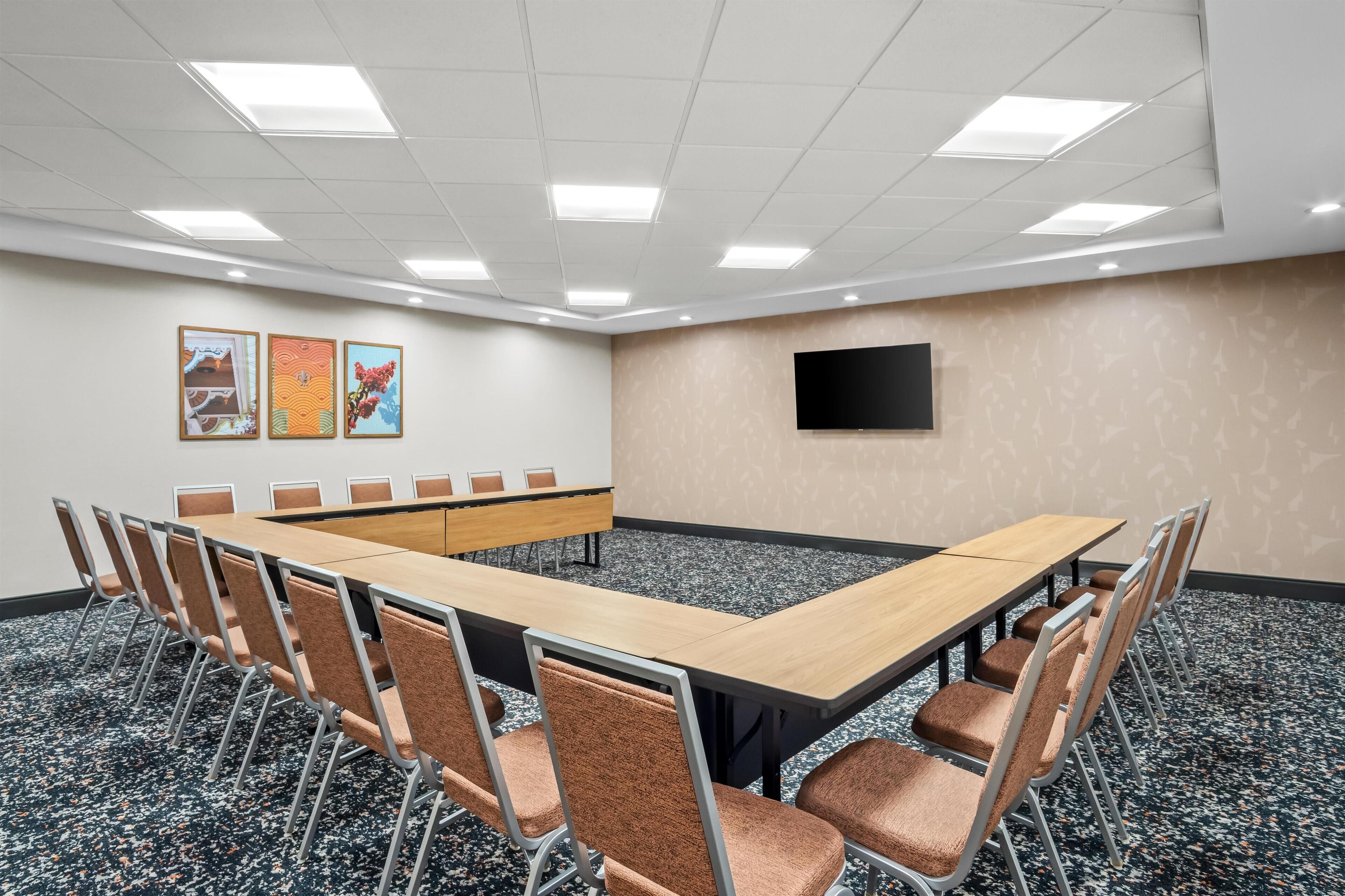Un salón de conferencias con una larga mesa, sillas, un televisor de pantalla plana y obras de arte en la pared.