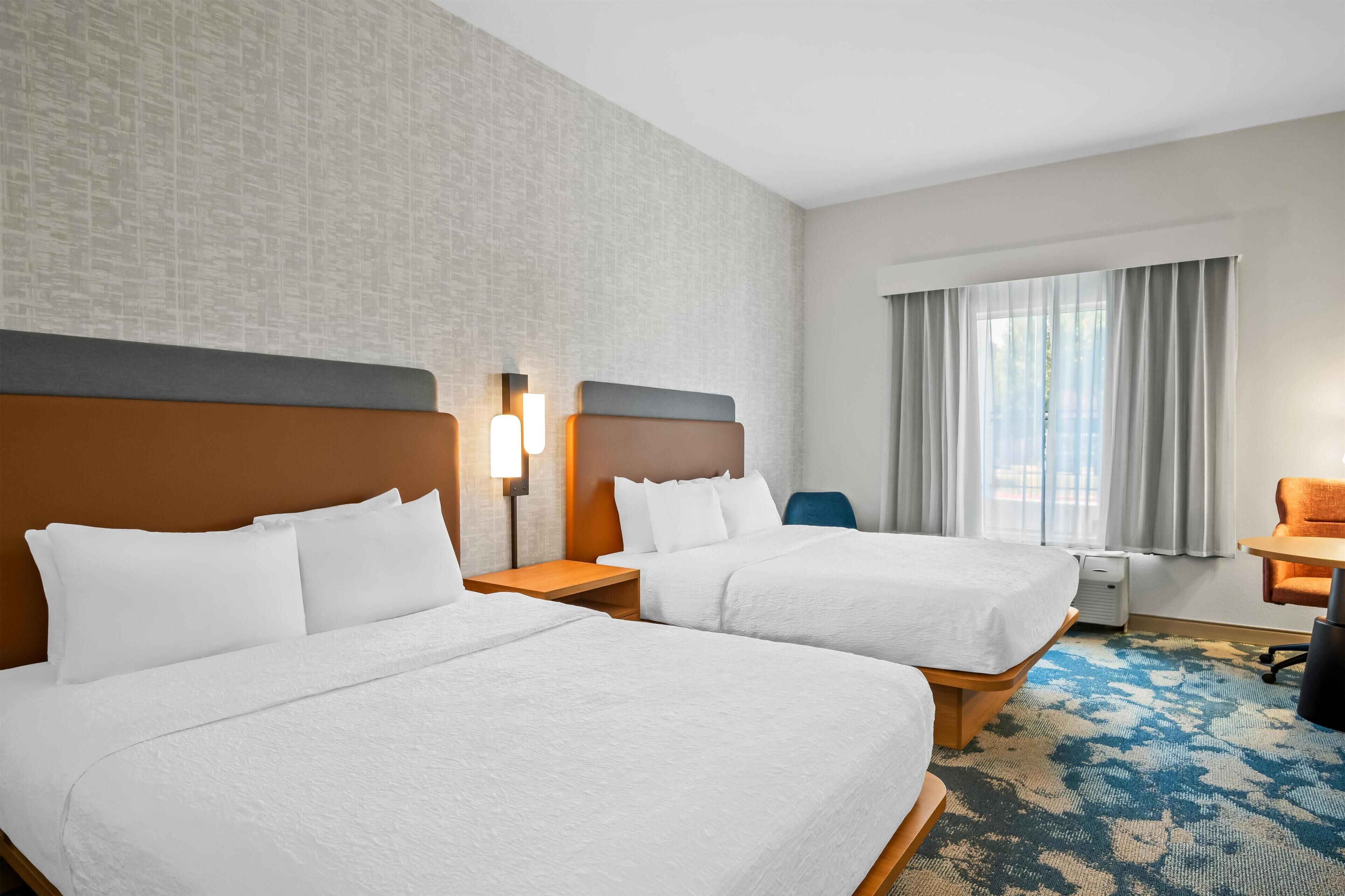 A hotel room with two beds, a desk, and a chair.
