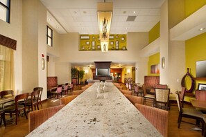 Un amplio vestíbulo de hotel con un largo mostrador de recepción de mármol, varias zonas de estar y una gran pantalla de televisión.