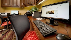 Un bureau d’hôtel équipé d’un ordinateur de bureau, d’un ordinateur portable, d’un clavier, d’une souris et d’une chaise avec un coussin à motifs rouges.