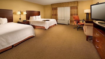 A hotel room with two beds, a desk with a computer, a TV, and a chair.