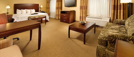 A hotel room with a bed, a desk, a sofa, a TV, and an air conditioning unit.