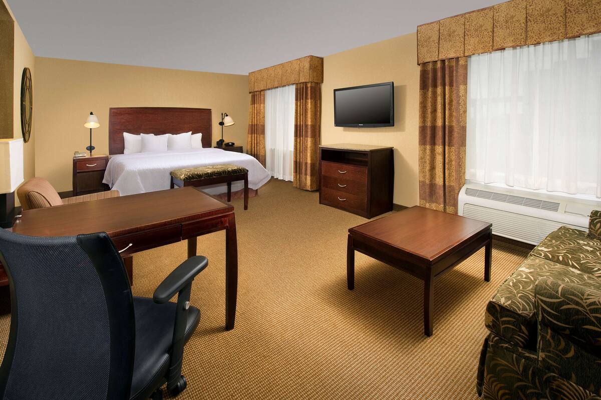 Una habitación de hotel con cama, escritorio, silla, televisor y sofá.
