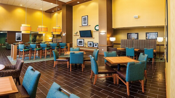 A hotel lobby with multiple seating areas, including tables and chairs, and a large clock on the wall.