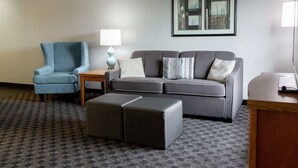 A modern living room with a grey sofa, a blue armchair, and a small wooden table with a lamp.