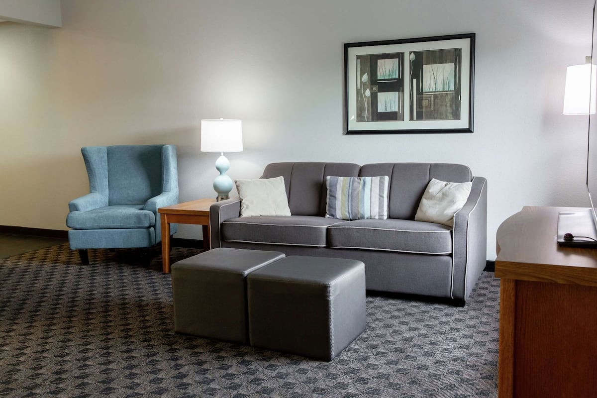 A hotel room with a grey sofa, a blue armchair, a small wooden table, and a patterned carpet.