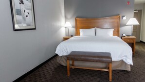 A neatly made bed with white linens, two bedside lamps, a wooden bench, and a framed picture on the wall.