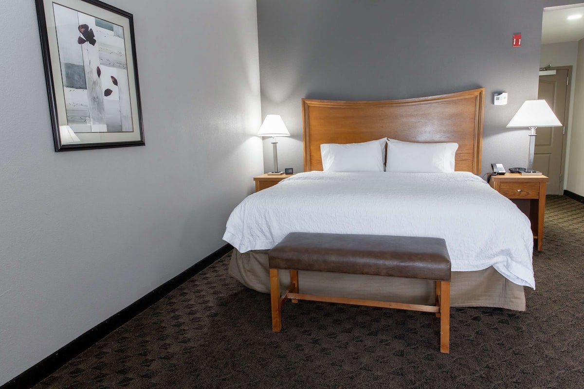 A neatly made bed with white linens, two bedside lamps, a wooden bench, and a framed picture on the wall.