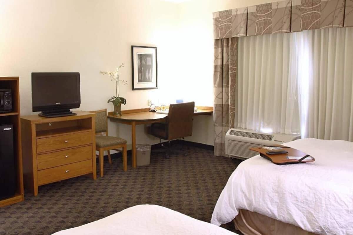A hotel room with a bed, a desk with a chair, a television, and a window with curtains.