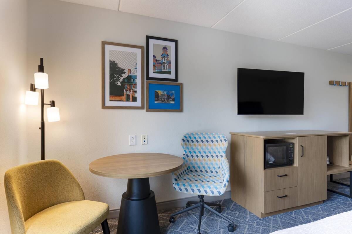Een hotelkamer met een bed, een bureau, een stoel, een televisie en een magnetron.