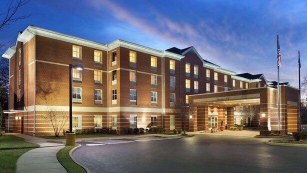 A multi-story hotel with a brick facade, a covered entrance, and a flagpole. - Hampton Inn & Suites Williamsburg Historic District (Williamsburg)