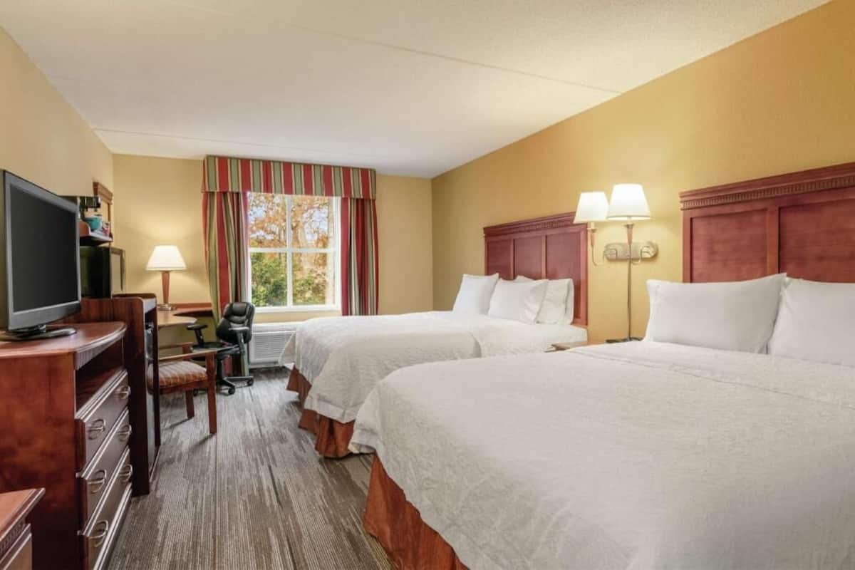 Een hotelkamer met twee bedden, een bureau met een computer, een televisie en een raam met gordijnen.