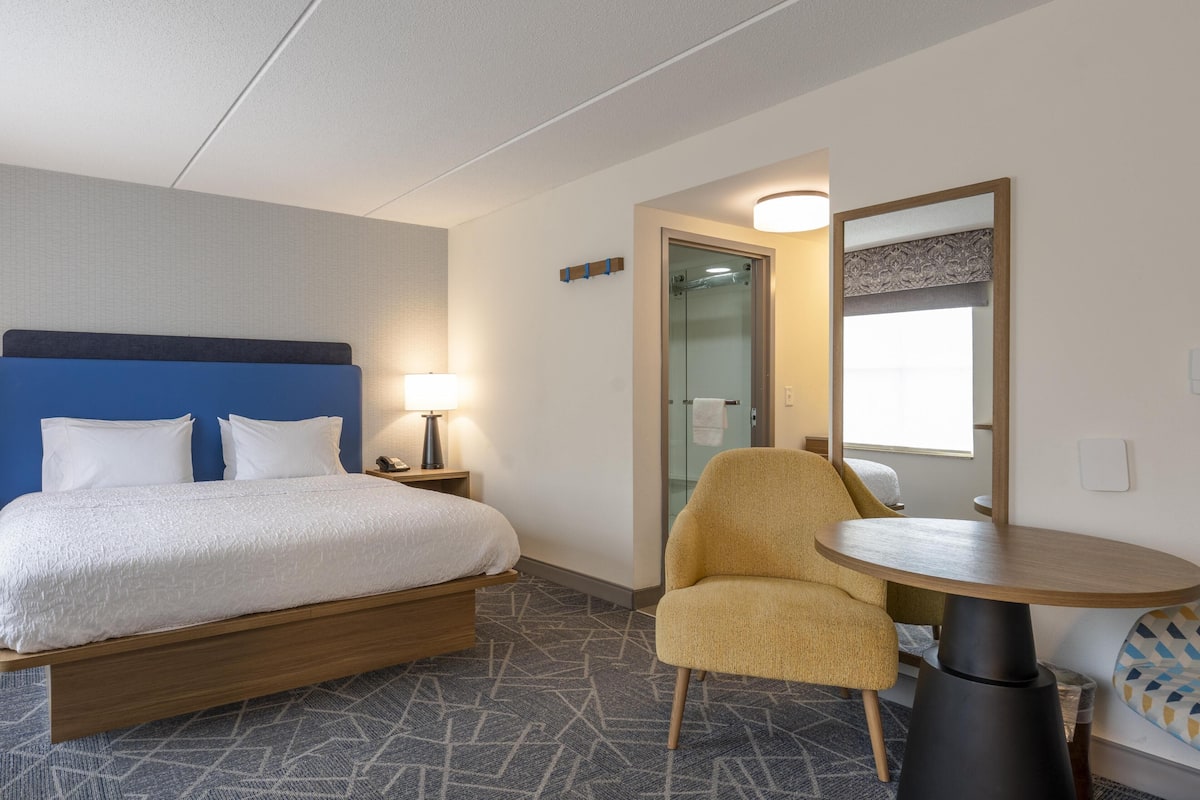 Een hotelkamer met een bed, een stoel, een ronde tafel en een spiegel.