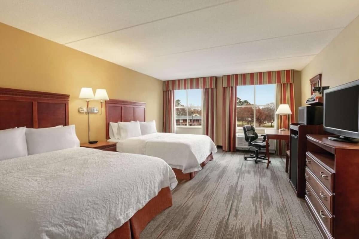 Een hotelkamer met twee bedden, een bureau, een televisie en uitzicht op de omgeving.