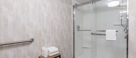 A modern bathroom with a glass shower enclosure, a towel rack, and a shelf with folded towels.