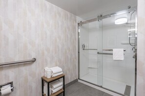 Une salle de bain moderne avec une douche à parois de verre, un porte-serviettes et une étagère où sont pliés les serviettes.
