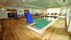An indoor swimming pool with wooden flooring, multiple lounge chairs, and a lifeguard sign. - Hampton Inn & Suites Williamsburg Historic District (Williamsburg)