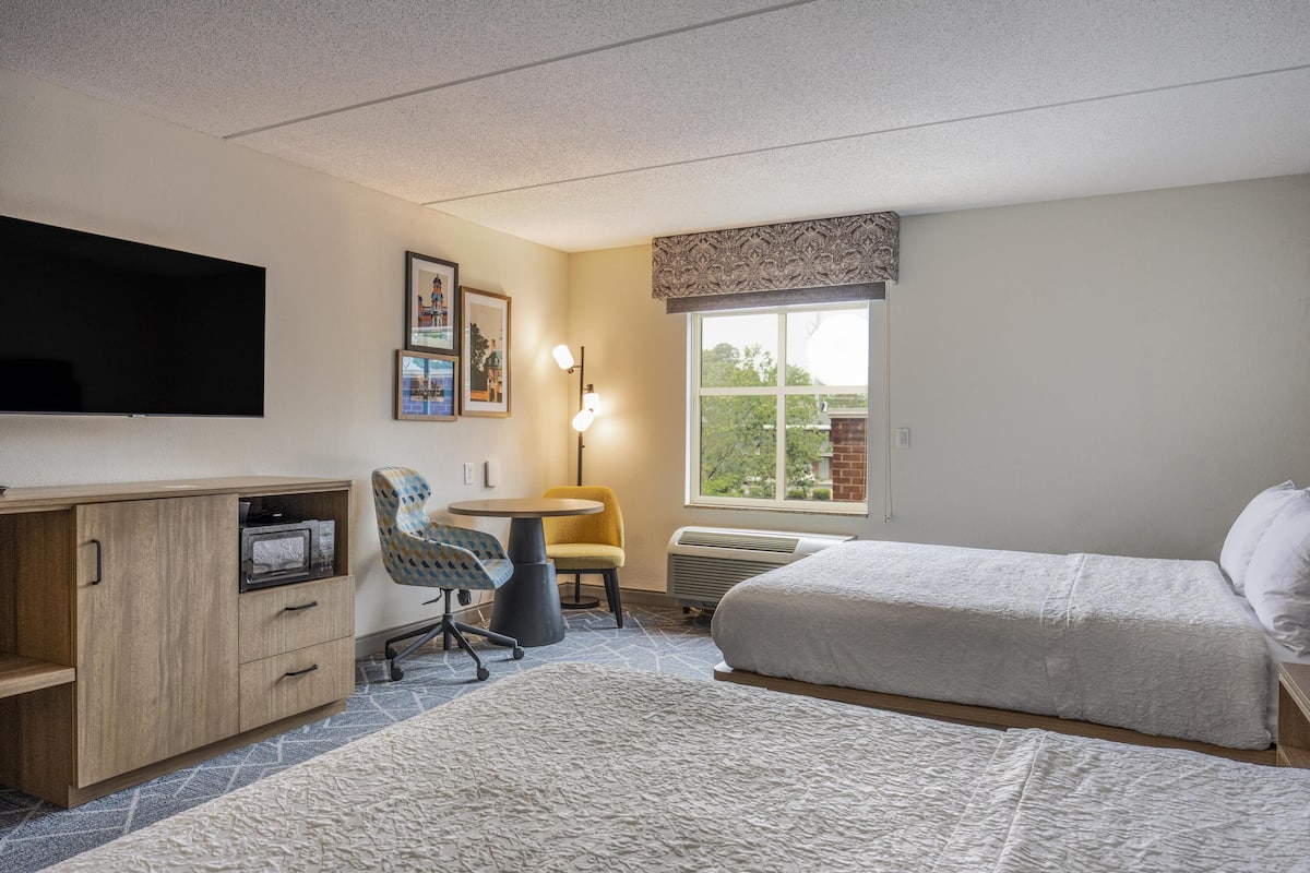 Een hotelkamer met een bed, een bureau met stoel, een flatscreen televisie, een raam met uitzicht en een wandradiator.