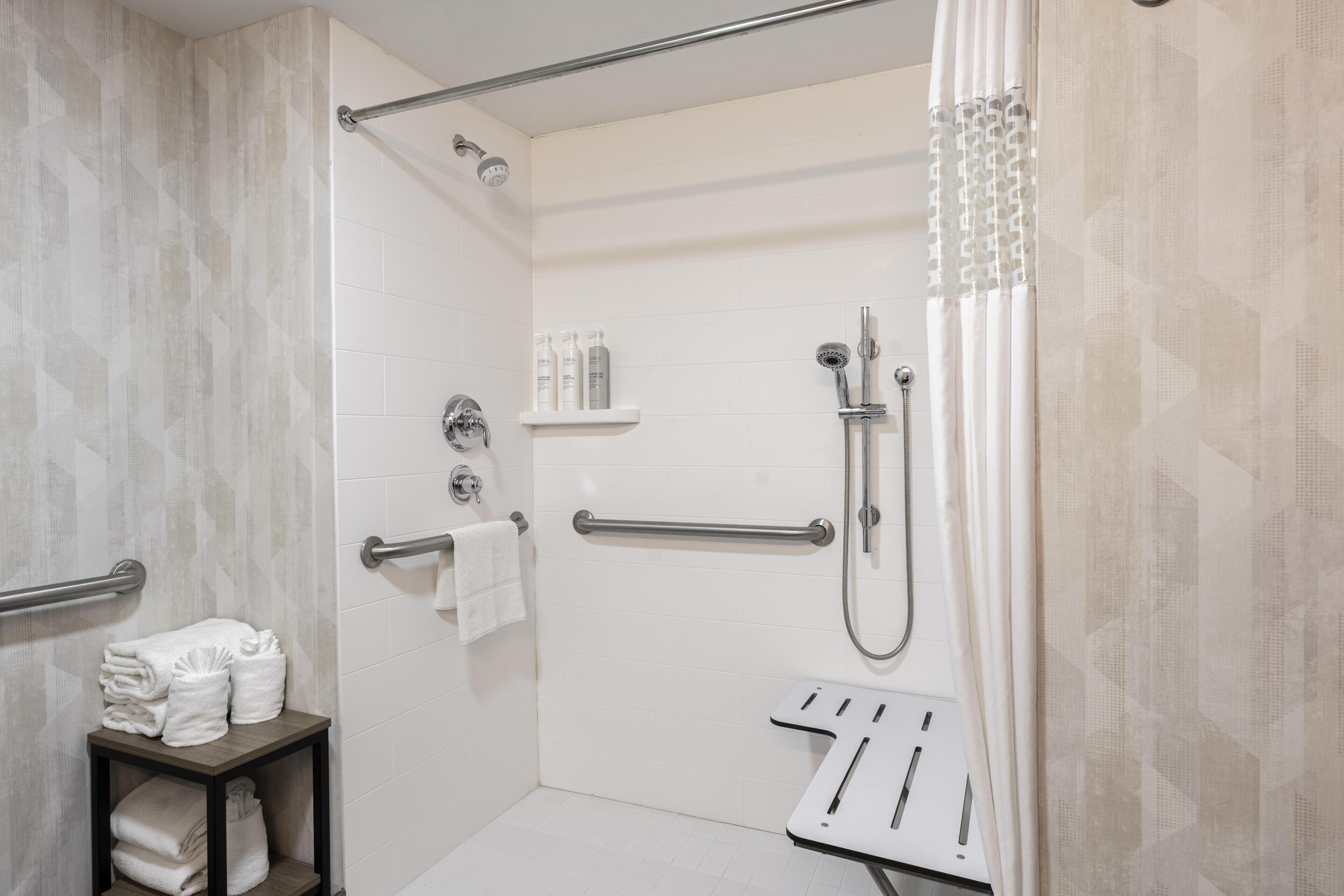 Un área de ducha con puerta de cristal, un perchero y un estante con artículos de aseo.