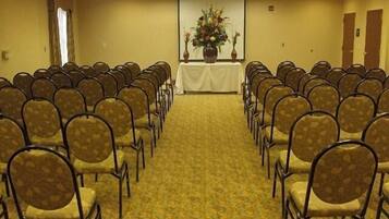 Un salón de conferencias con filas de sillas orientadas hacia un atril con un arreglo floral.