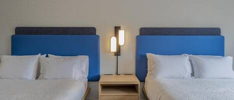Habitación de hotel con dos camas, una mesita de noche con lámpara y una alfombra estampada.