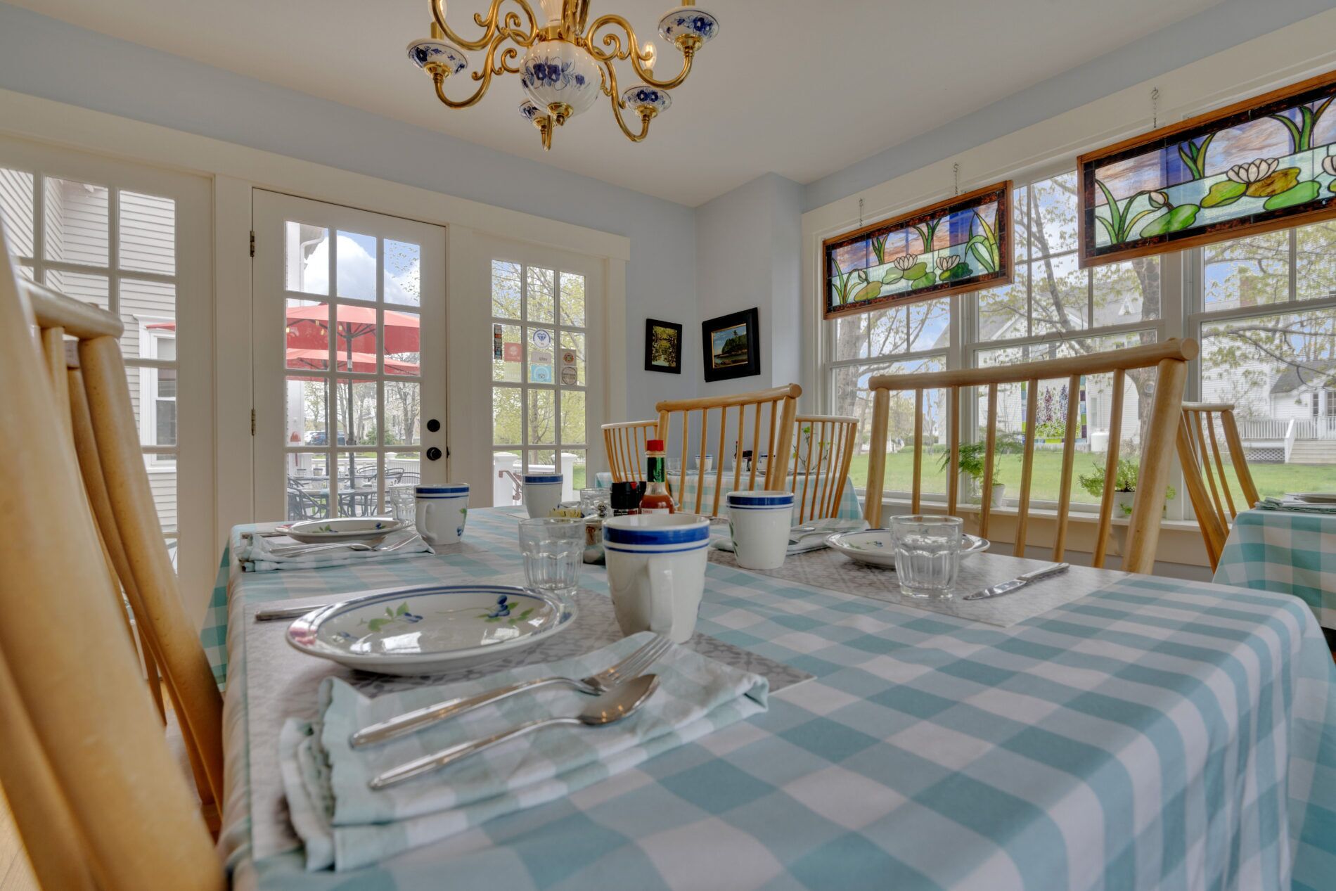 A dining area with a checkered tablecloth, a chandelier, and a view of the outdoors through large windows.